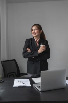 Portrait of young confident woman holding coffee cup, standing at office and looking outside. Successful businesswoman standing in office with copy space..