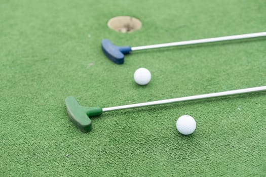 Mini-golf clubs and balls of different colors laid on artificial grass. High quality photo