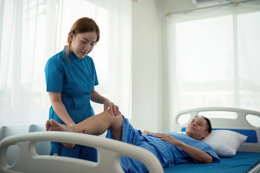 Physical therapist Asian woman, doing leg physiotherapy for elderly man to treat osteoarthritis and nerve pain in the leg to nursing at home and health care concept.