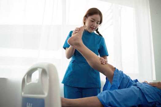 Physical therapist Asian woman, doing leg physiotherapy for elderly man to treat osteoarthritis and nerve pain in the leg to nursing at home and health care concept.