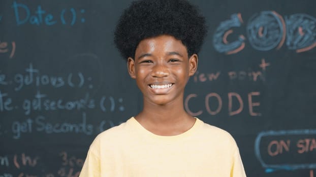 African adult smiling to camera while standing at blackboard with engineering code or prompt. Closeup of handsome teenager wearing casual cloth while attend in STEM technology class. Edification.