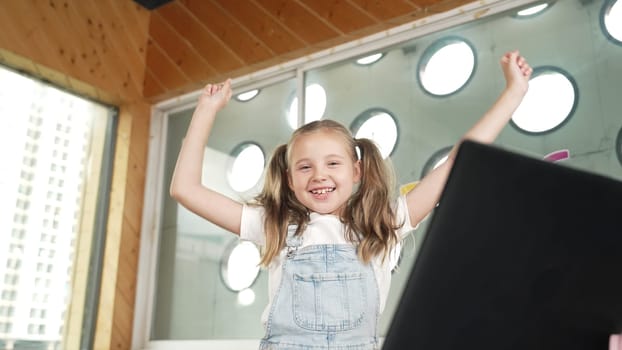 Happy girl looking at camera while raised hands to celebrate success project. Smart cute student finish writing, programing system and shouting with happiness in STEM technology class work. Erudition.