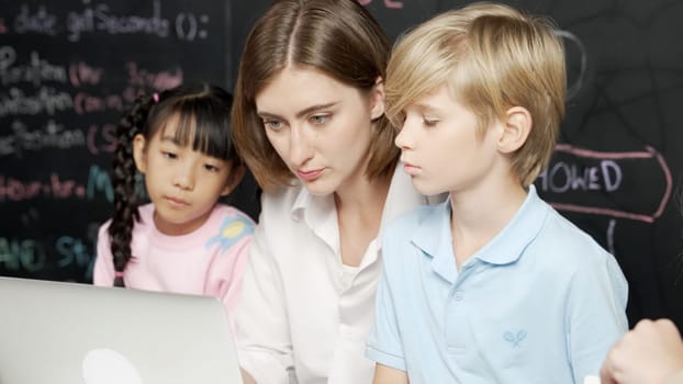 Young smart teacher using laptop to teach diverse student programing system. Caucasian learner looking at computer screen while study about coding prompt at blackboard with program code. Erudition.