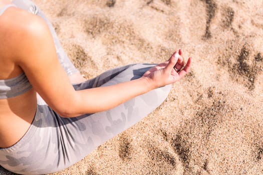 detail of the hand and leg of an unrecognizable woman doing meditation sitting on the beach sand, concept of mental relaxation and healthy lifestyle