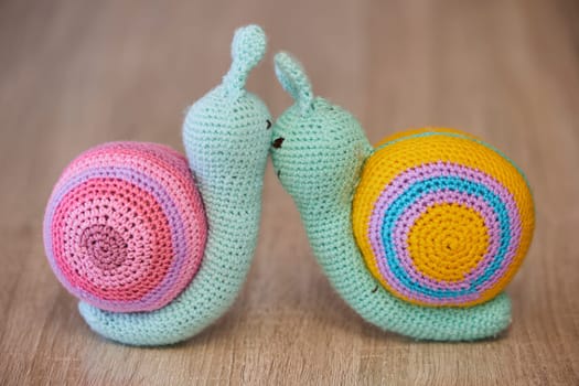 Cute knitted toy snails kissing like a married couple.
