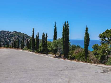 Beautiful panoramic view of a straight asphalt road in a coniferous forest on Mount Filerimos overlooking the Aegean Sea in Greece on a sunny summer day, side view close-up.