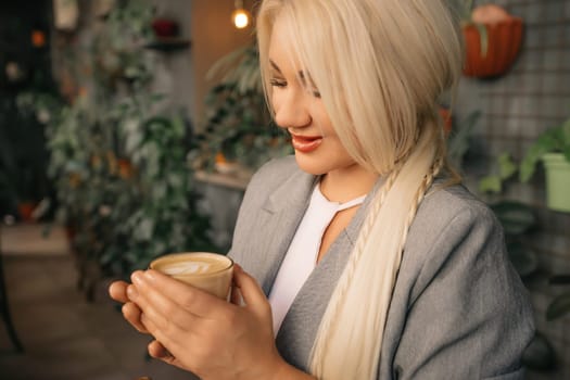 A person is holding a cup of coffee and looking at it. The coffee is hot and has a creamy foam on top. The person is wearing a suit and tie, and there are other people in the background