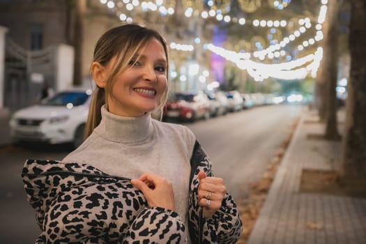 A woman wearing a leopard print jacket is smiling in front of a car. The scene is set in a city at night, with lights and cars visible in the background. The woman is enjoying her time
