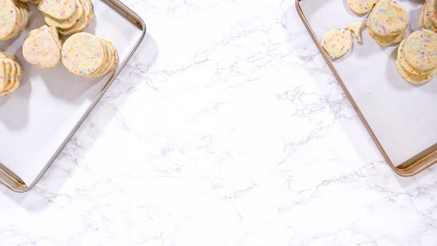 Flat lay. With precision, the woman is carefully arranging the sugar cookies, filled with dough-mixed sprinkles, into a rustic brown paper box.