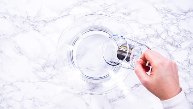 Flat lay. A spacious glass mixing bowl filled with water sits prepared to gently cleanse a batch of ripe strawberries, ensuring they are pristine before drying or storage.