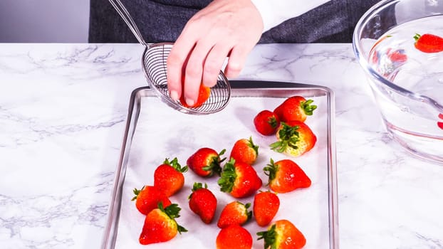 Juicy red strawberries, freshly washed, are spread out to dry on a baking sheet, carefully lined with paper towels to absorb excess moisture and prevent mold.