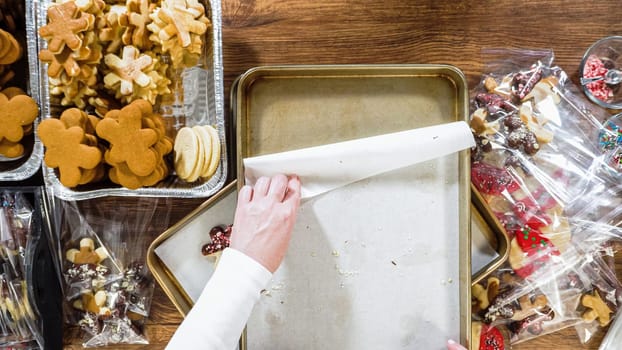 Flat lay. Carefully packaging Christmas cutout cookies, half-dipped in chocolate, sprinkled with crushed nuts, and presented in clear cellophane wrapping.