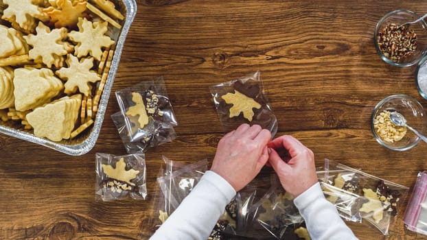 Flat lay. Carefully packaging Christmas cutout cookies, half-dipped in chocolate, sprinkled with crushed nuts, and presented in clear cellophane wrapping.