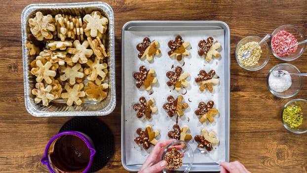 Flat lay. Creating snowflake-shaped cutout sugar cookies, dipped in chocolate, and adorned with different toppings.