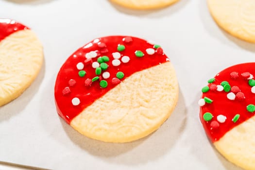 Skillfully decorating cookies with vibrant red melted chocolate and a generous sprinkle of vibrant green, creating a festive holiday treat.