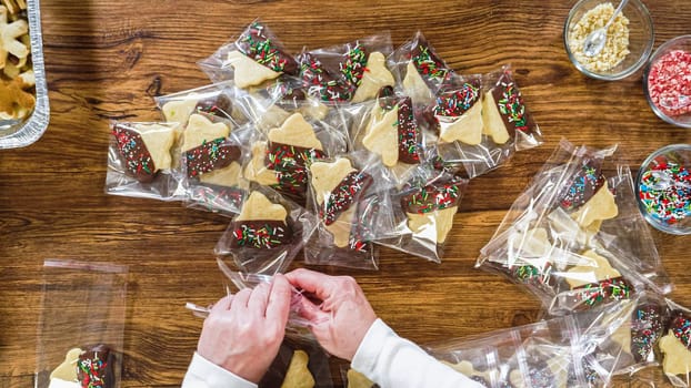 Flat lay. Carefully packaging Christmas cutout cookies, half-dipped in chocolate, sprinkled with crushed nuts, and presented in clear cellophane wrapping.