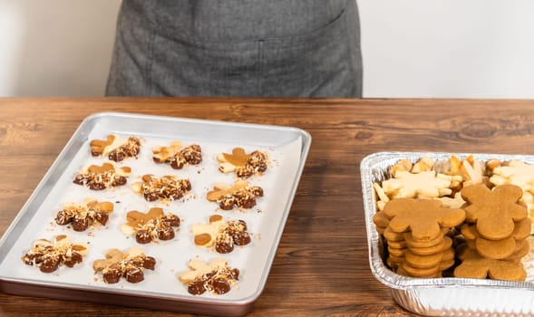 Gingerbread men cookies, chocolate-dipped feet, generously sprinkled with golden toasted coconut shavings, artfully arranged on parchment paper.