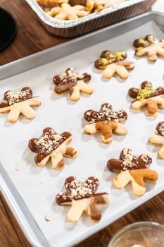 Creating cutout sugar cookies, partially dipped in chocolate and topped with hazelnut pieces, placed on parchment paper.