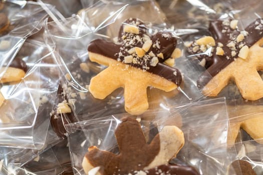 Carefully packaging Christmas cutout cookies, half-dipped in chocolate and presented in clear cellophane wrapping, perfect for festive gifting.