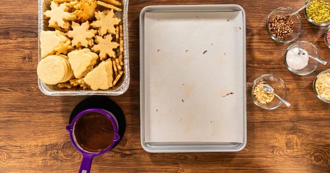 A delightful holiday baking setup featuring a variety of cookies, bowls of melted chocolate, an assortment of nuts, and an array of colorful toppings, all prepared and ready for festive decorating.