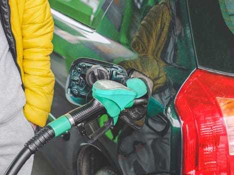 A young unrecognizable Caucasian man in a yellow jacket and gray tracksuit fills up his car with gasoline, close-up side view. The concept of refueling cars with gasoline.