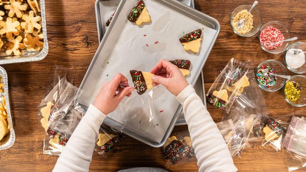 Carefully packaging Christmas cutout cookies, half-dipped in chocolate and presented in clear cellophane wrapping, perfect for festive gifting.