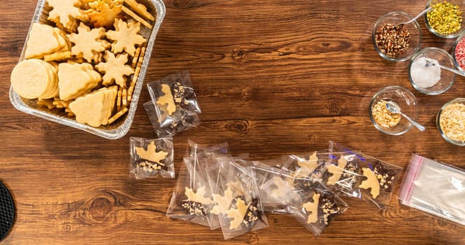 Carefully packaging Christmas cutout cookies, half-dipped in chocolate, sprinkled with crushed nuts, and presented in clear cellophane wrapping.