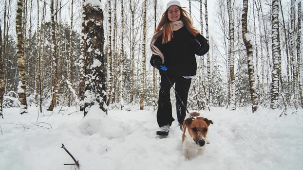 A girl and her Jack Russell Terrier dog are running through the woods