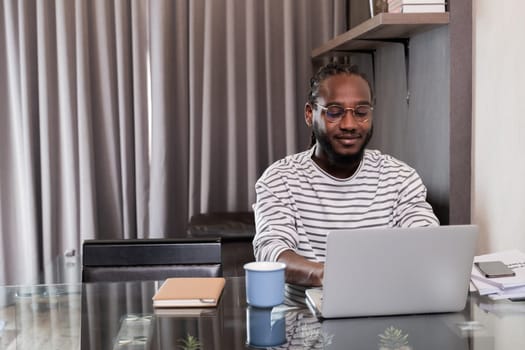 Young African American businessman spends his weekend working from home using his laptop in the living room..