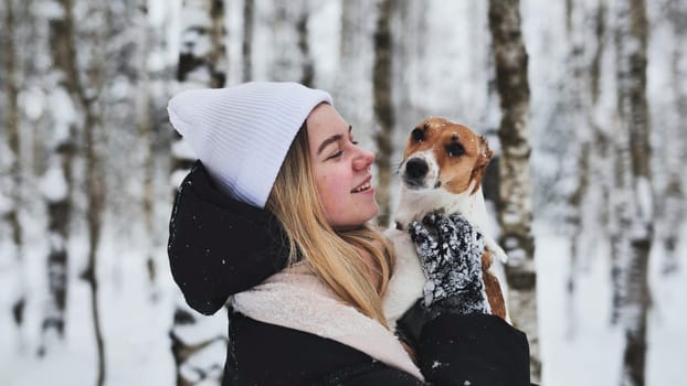 A girl cuddles a Jack Russell Terrier dog in the woods in winter