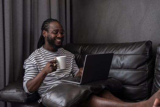 Young African American businessman spends his weekend working from home using his laptop in the living room..