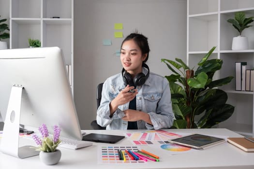 Female designer wearing headphones listening to music while doing graphic design work Choose colors for working with the computer at the table..