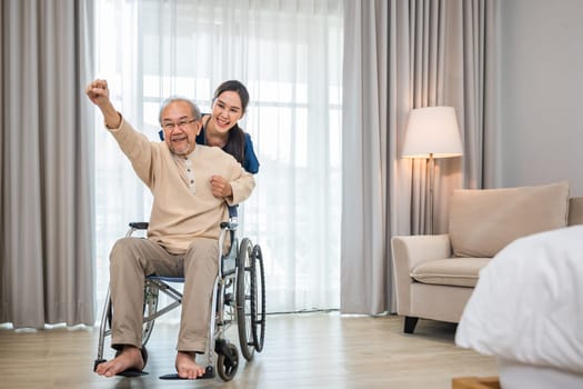 Asian senior retired old man sitting on wheelchair having fun with young woman nurse, Happy curator person doctor pushing and running elderly patient freedom raising arm, sanatorium