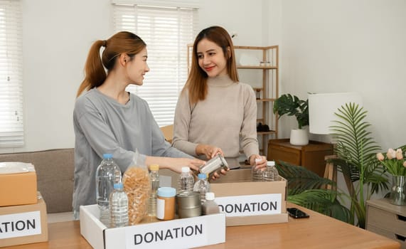 Two young female volunteers help pack food into donation boxes and prepare to donate them to charity..