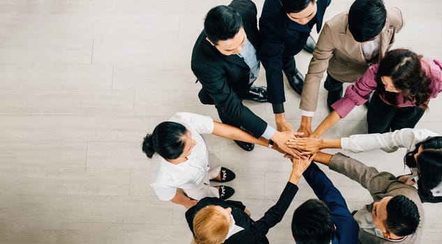 Aerial perspective of four diverse professionals in a circle hands stacked in unity. This image symbolizes teamwork trust and global cooperation in the corporate environment.