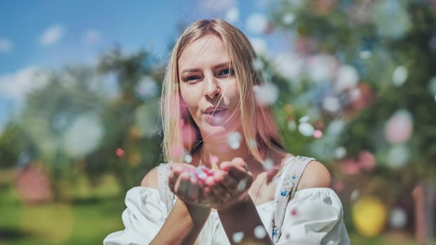 A girl blows a multi-coloured paper confetti out of her hands