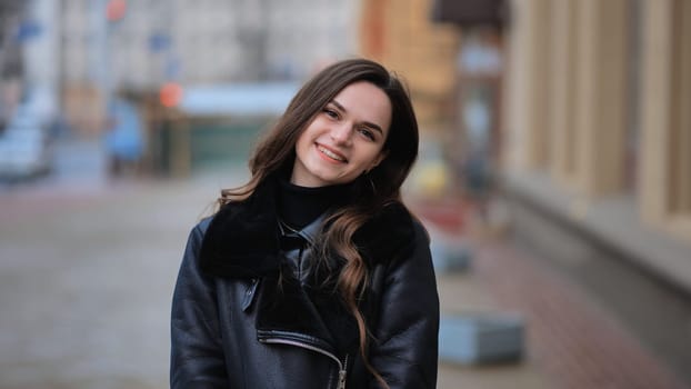 Happy brunette girl posing in black jacket in autumn in the city