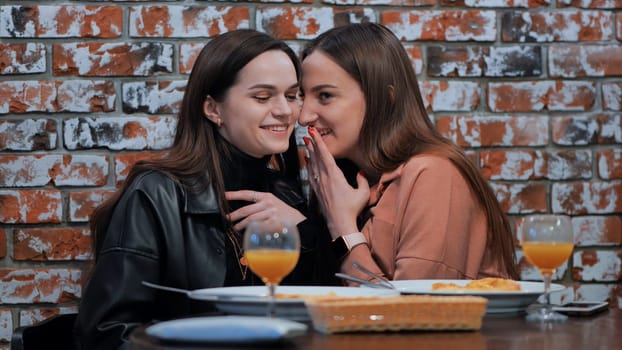 Two young girls gossiping sitting in a cafe