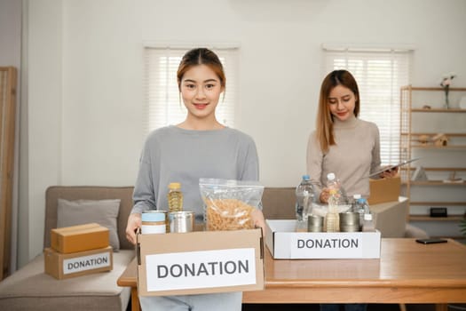 Beautiful female volunteer holds a donation box with canned food in it..