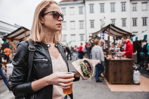 Close up of woman hands holding delicious organic salmon vegetarian burger and homebrewed IPA beer on open air beer an burger urban street food festival in Ljubljana, Slovenia