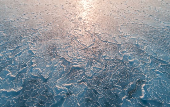 Aerial top down view of ice surface. Frozen sea surface texture with sun reflection