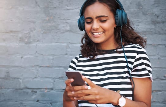 Girl, headphones and cellphone with wall background in city for music listening, subscription or podcast. Female person, smile and urban town with technology for internet app, playlist or streaming.