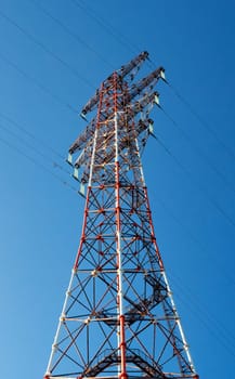 Bottom view of a high-voltage electricity pylon against blue sky at sunny day. High-voltage power transmission tower. Power engineering.