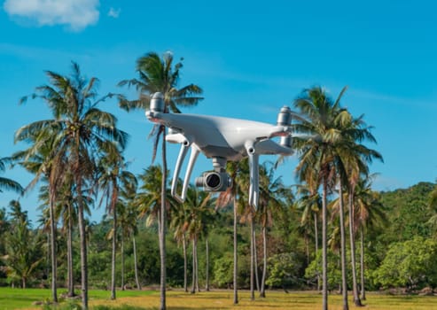 White drone quadrocopter flying against the background of a tropical trees, close-up shot
