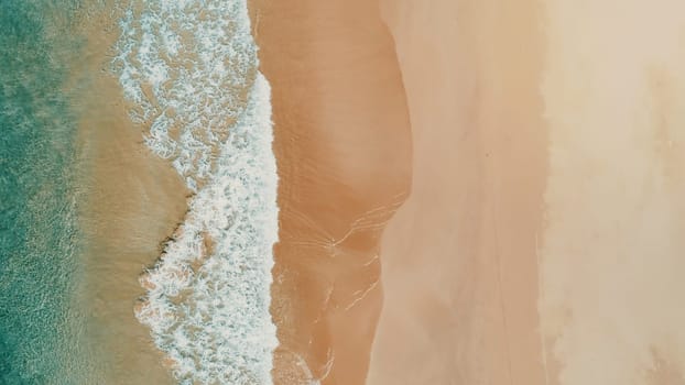 Aerial top view of turquoise ocean wave reaching the coastline.