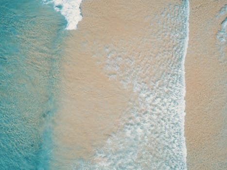 Aerial top view of turquoise ocean wave reaching the coastline.