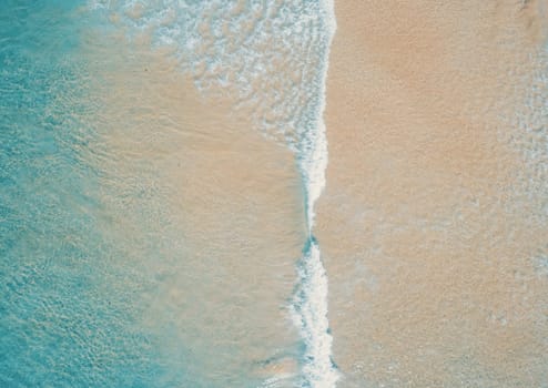 Aerial top view of turquoise ocean wave reaching the coastline.