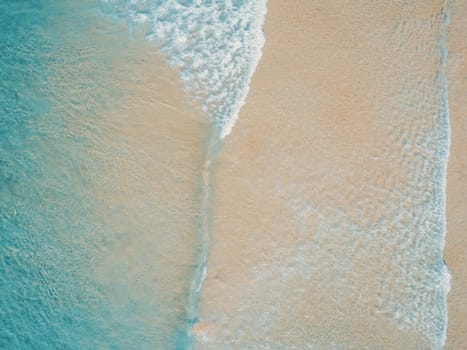 Aerial top view of turquoise ocean wave reaching the coastline.