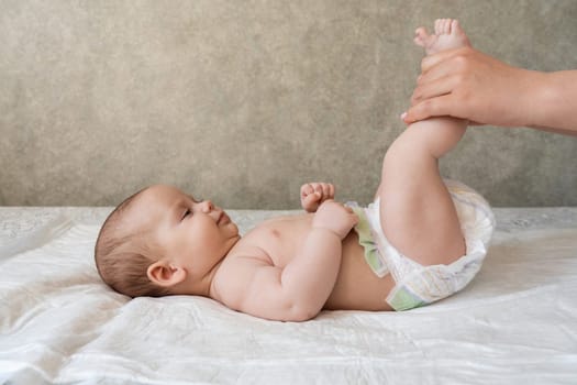 Mother's hands hold and caress baby legs, applying massage to promote health and comfort