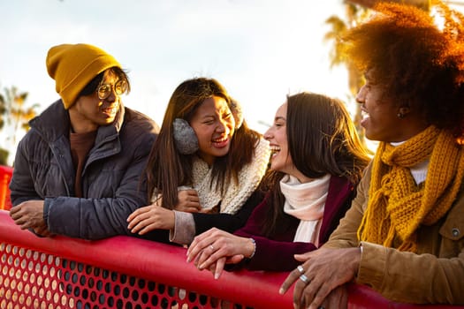 Happy multiracial college student friends laughing and talking enjoying sunny winter day. Multiethnic people having fun together outdoors in city. College student and lifestyle concept.